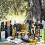 photo of different olive oils on a table under a very old olive tree