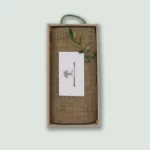 The inside of a Gourmet Groceries gift box, with products under a linen wrapping, a card, and an olive leaf.