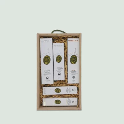 A wooden gift box containing various Marfuga Bio Cosmetics skincare products. The products are arranged neatly in wood wool and include body wash, nourishing oil, shampoo, hand and face cream. The box has a green rope handle.