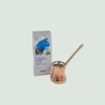 A package of Nektar Traditional Greek Coffee and a copper cezve with a long handle. The coffee package is white with blue accents, and the cezve has a hammered texture.