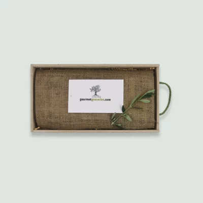 The inside of a Gourmet Groceries gift box, with products under a linen wrapping, a card, and an olive leaf.
