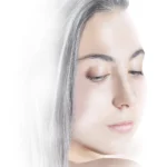 A woman applying OLIAURA Repairing and Toning Face Cream to her face, demonstrating the product's smooth texture and hydrating properties.