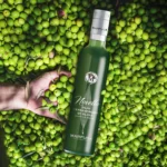 A bottle of Marfuga Novello Extra Virgin Olive Oil nestled among freshly picked olives, highlighting its premium quality and natural origins.