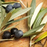 A handful of Lavandia's dried olive tree leaves on a wooden surface, highlighting their organic quality and traditional preparation.