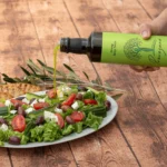 Prevezana Greek Olive Oil being drizzled over a vibrant salad, highlighting its rich texture and aromatic flavor.