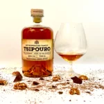 A distiller testing aged Spyropoulos Tsipouro in a glass, showcasing its golden color and clarity.