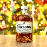 Spyropoulos Aged Tsipouro bottle illuminated against a backdrop of warm decorative lights, emphasizing its premium design.