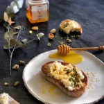 A slice of bread topped with Vasilissa Wildforest Honey, showcasing its delicious golden drizzle and inviting appearance for a perfect breakfast treat.
