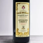 Giusti Balsamic Vinegar of Modena on a wooden kitchen counter next to fresh vegetables and bread.