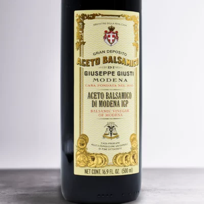 Giusti Balsamic Vinegar of Modena on a wooden kitchen counter next to fresh vegetables and bread.