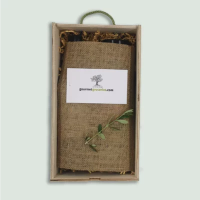 The inside of a Gourmet Groceries gift box, with products under a linen wrapping, a card, and an olive leaf.